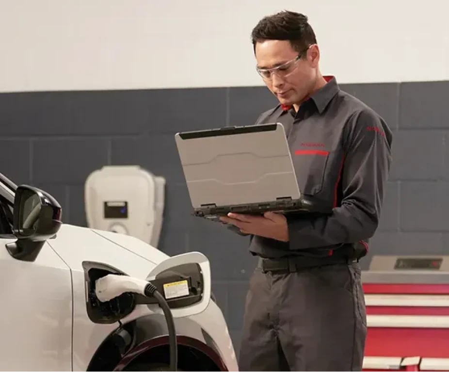 Nissan technician using a diagnostic laptop near an electric vehicle charging port