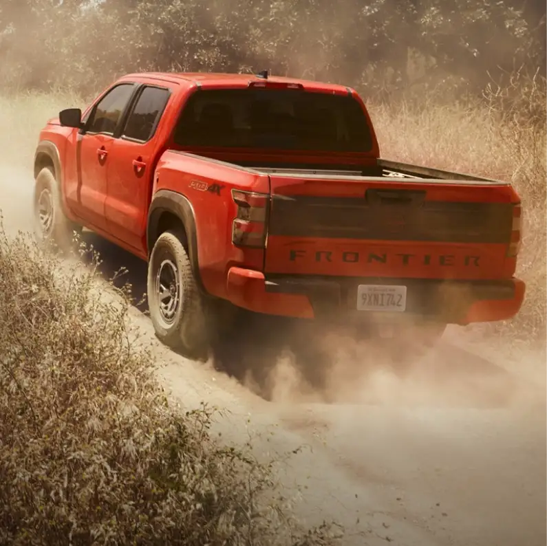 Orange Nissan Frontier driving on a dusty off-road trail