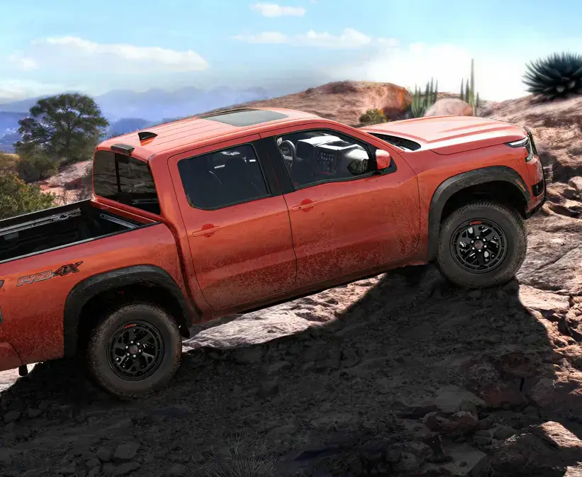 Orange Nissan truck climbing a rocky mountain trail