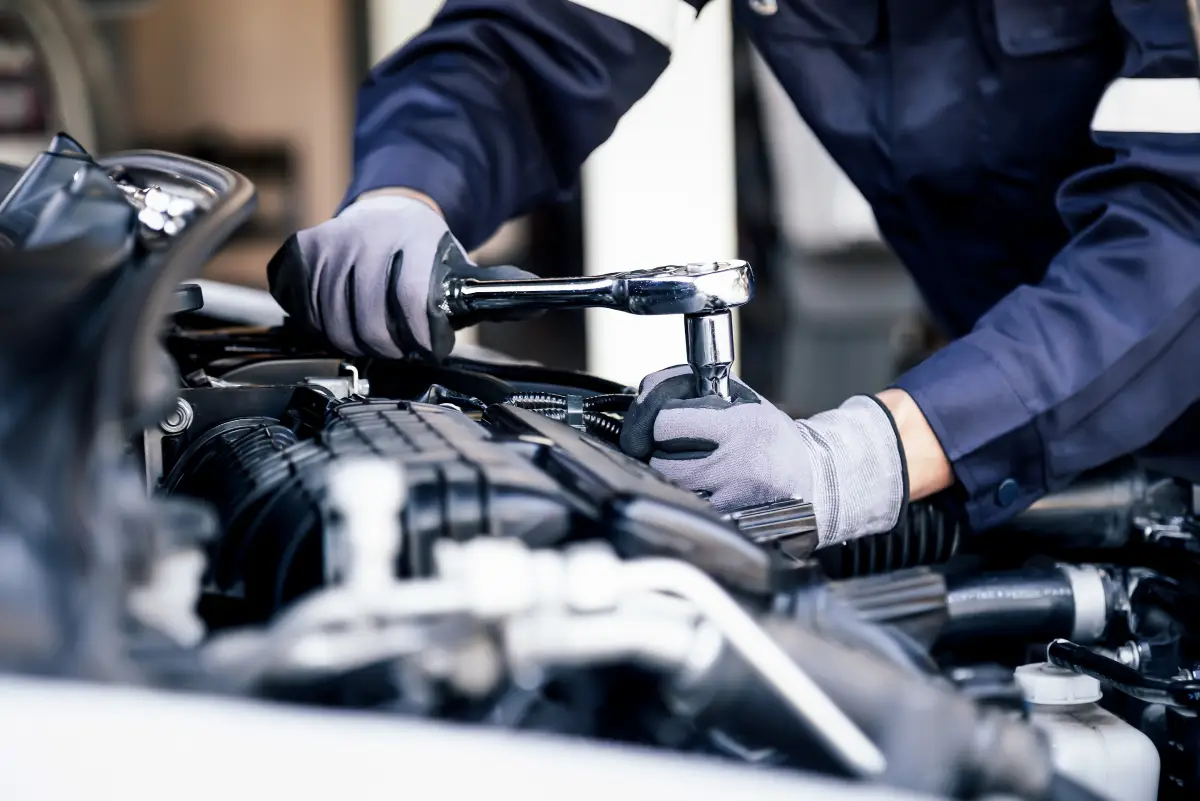 Mechanic in gloves using a ratchet on a car engine during vehicle repair at Aros Automotive in Gainesville, GA