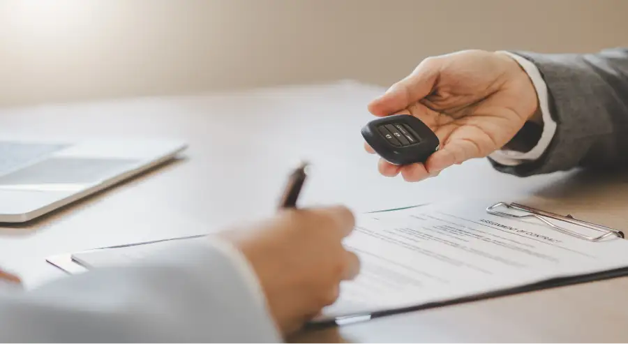 Customer signing car loan paperwork and receiving the keys to their new vehicle at Auto Sense North