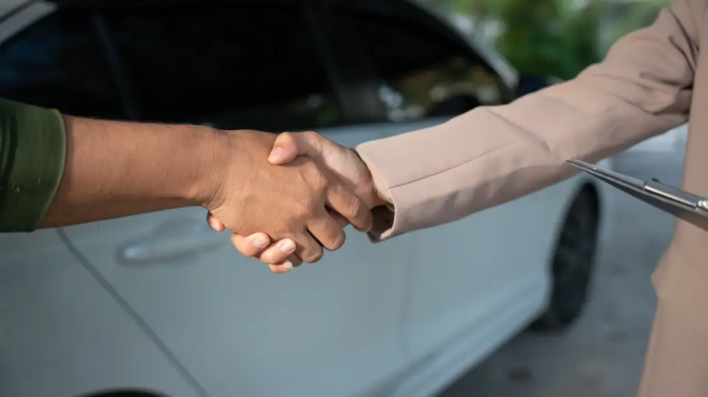 Customer and dealership representative shaking hands during vehicle delivery