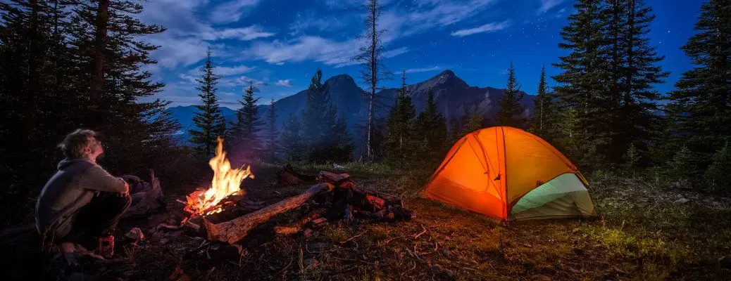 Man looking up at the stars next to campfire and tent at night