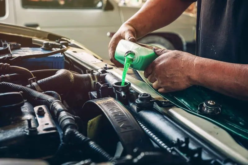 Male professional mechanic pouring antifreeze coolant liquid into car engine radiator in service center, car repair shop. Concept of car radiator coolant maintenance