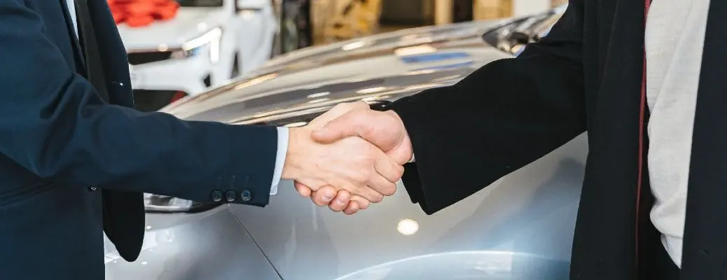Two men shaking hands in front of a car, as a means of illustrating where to finance a car near Dallas.