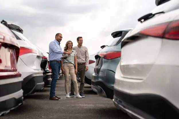 Car salesman assisting a couple choosing a pre-owned vehicle at a car dealership lot