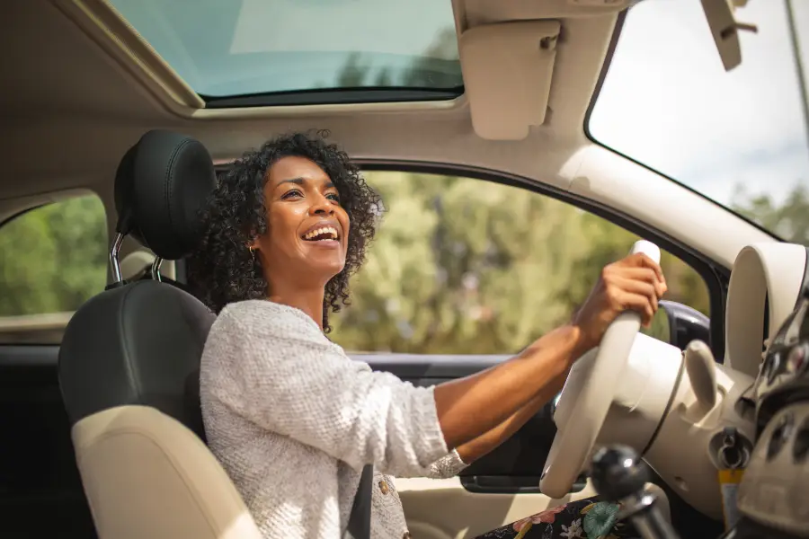 Smiling driver sitting in the front seat of a car with a sunroof, holding the steering wheel and looking ahead.