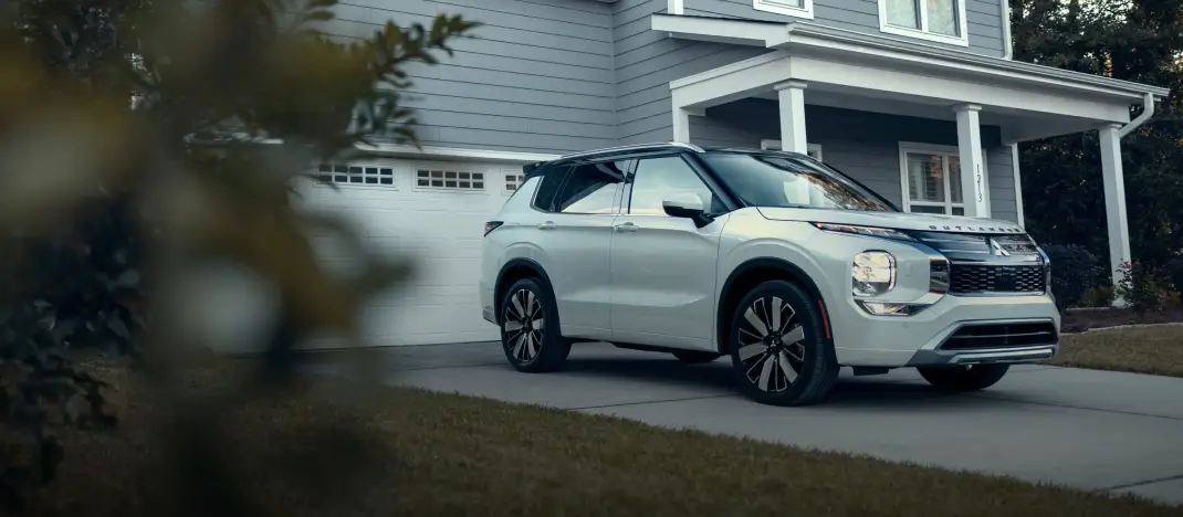 White Mitsubishi Outlander parked outside a home for the Mitsubishi Certified Pre-Owned program.
