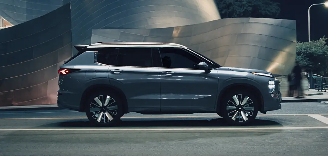 Gray Mitsubishi Outlander driving through a city street at night.