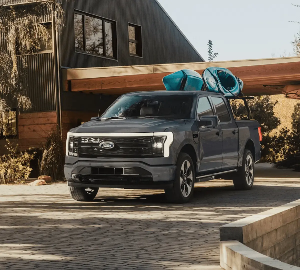 Gray Ford F-150 Lightning with kayaks on a roof rack parked outside a modern home