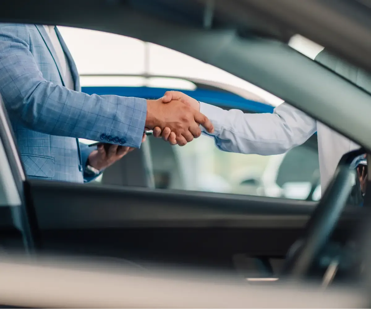 Customer shaking hands with a dealership representative during a vehicle purchase.