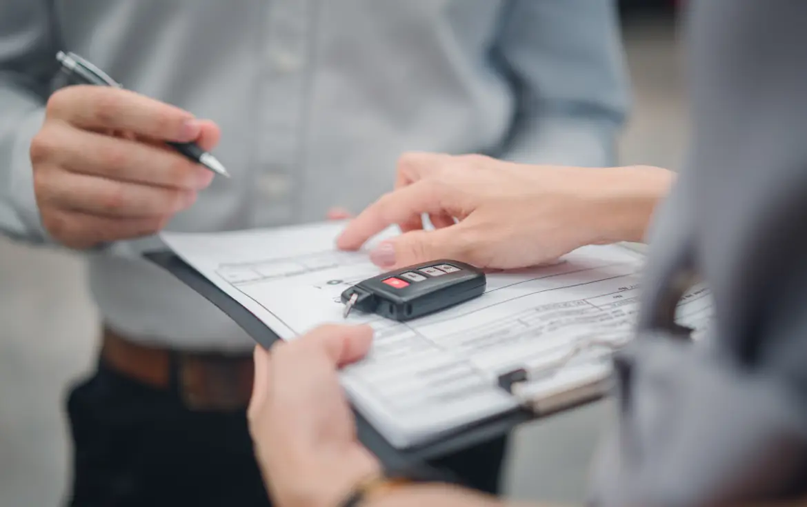 Person signing vehicle purchase documents with a car key fob on a clipboard.