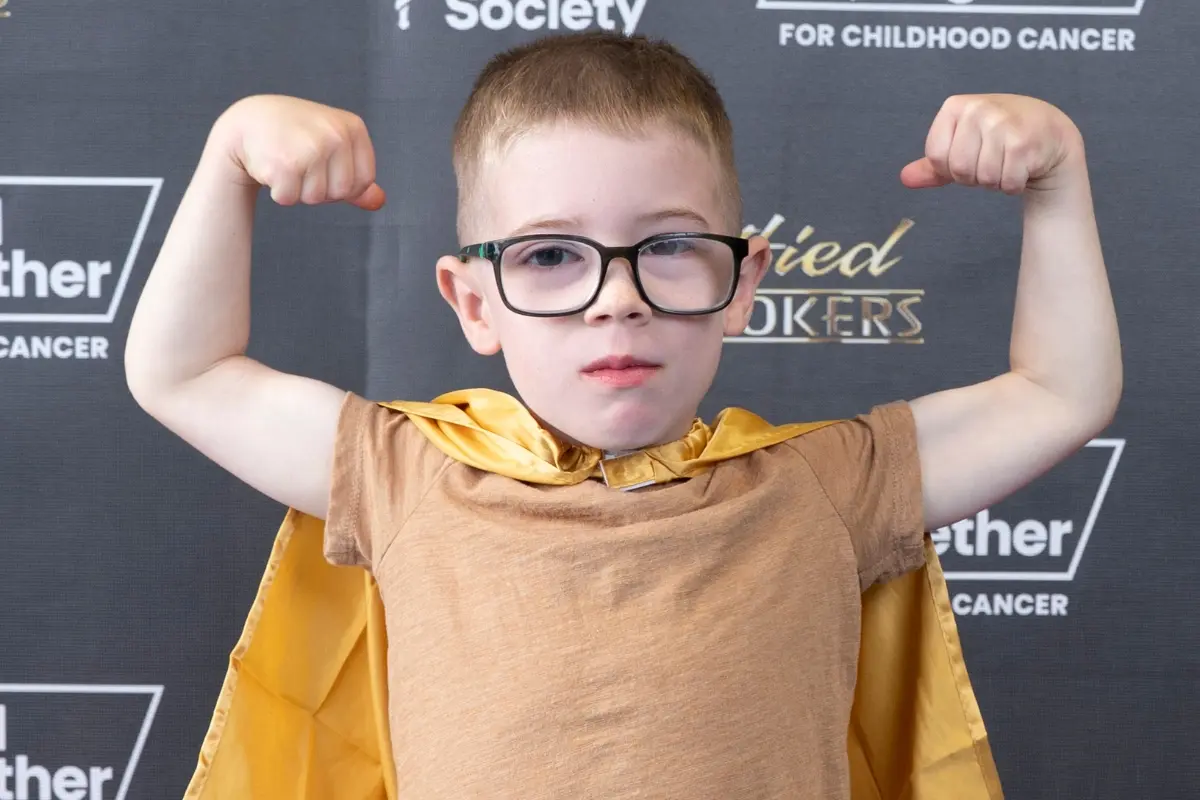 Child in a gold superhero cape at the Gold Together for childhood cancer backdrop during Drive for a Cure at Certified AutoBrokers in Grand Island NY