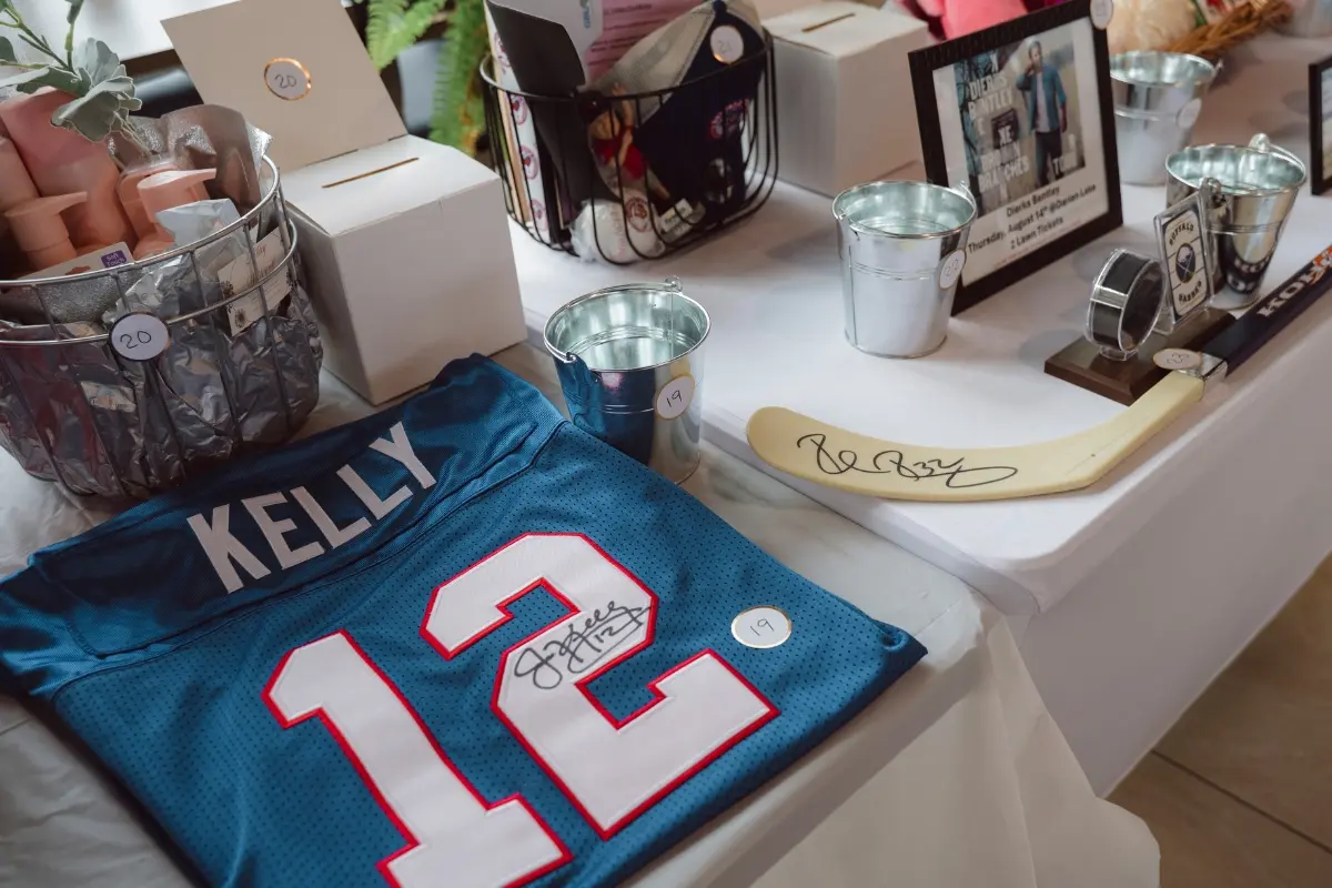 Raffle prize table featuring a signed Jim Kelly jersey and gift baskets at the Drive for a Cure event at Certified AutoBrokers in Grand Island NY