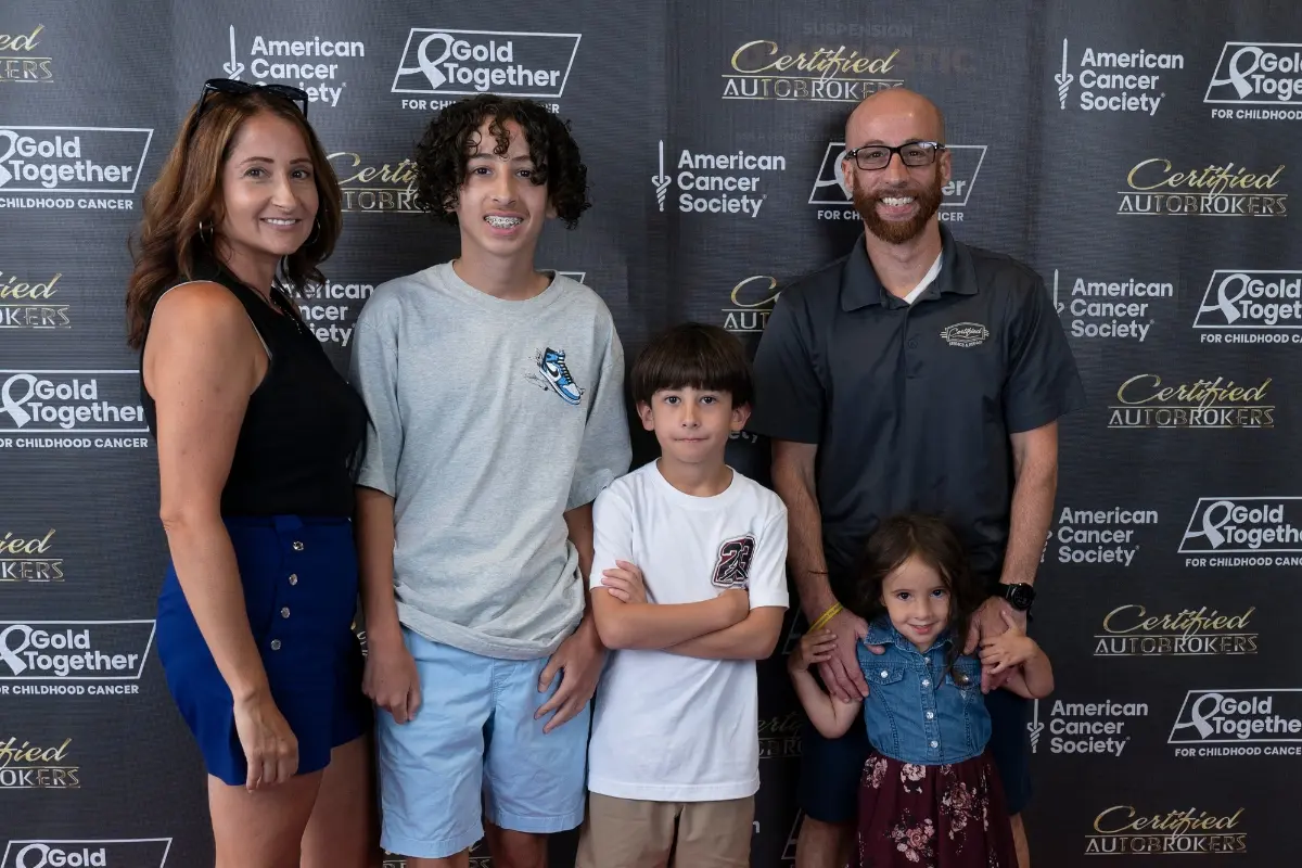 Family posing at the Gold Together and American Cancer Society backdrop during the Drive for a Cure event at Certified AutoBrokers in Grand Island NY