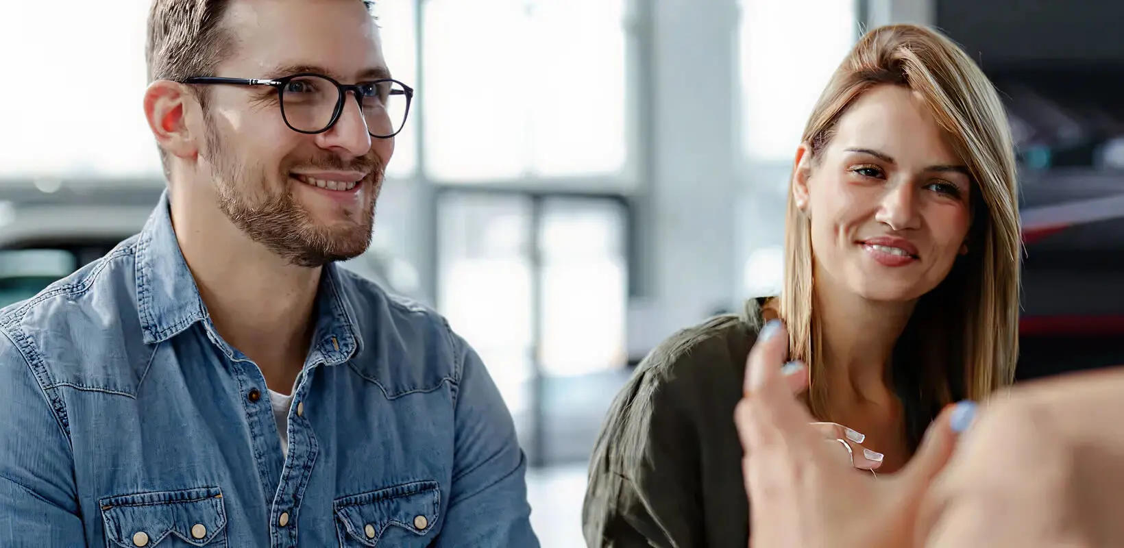 Two customers smile at a desk with a salesperson.