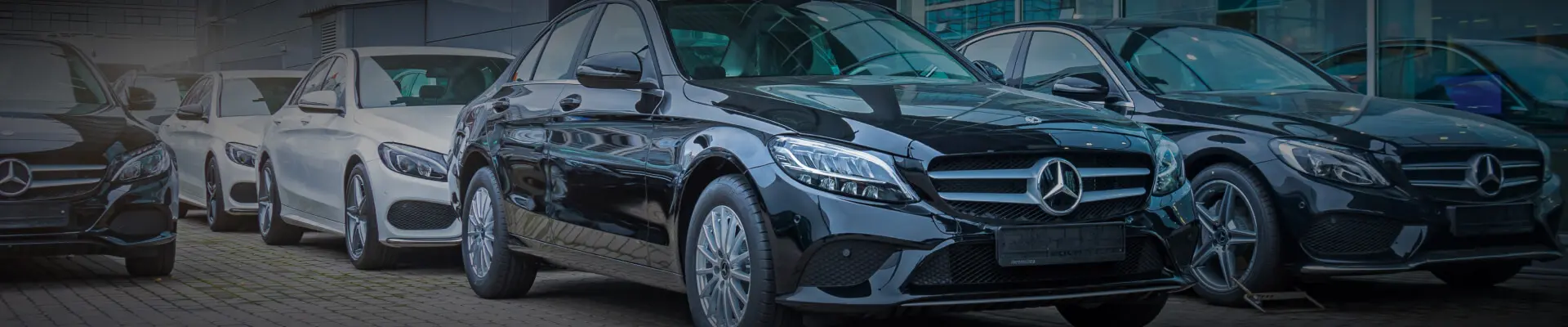 A lineup of Mercedes-Benz cars parked outside a bright, modern dealership.