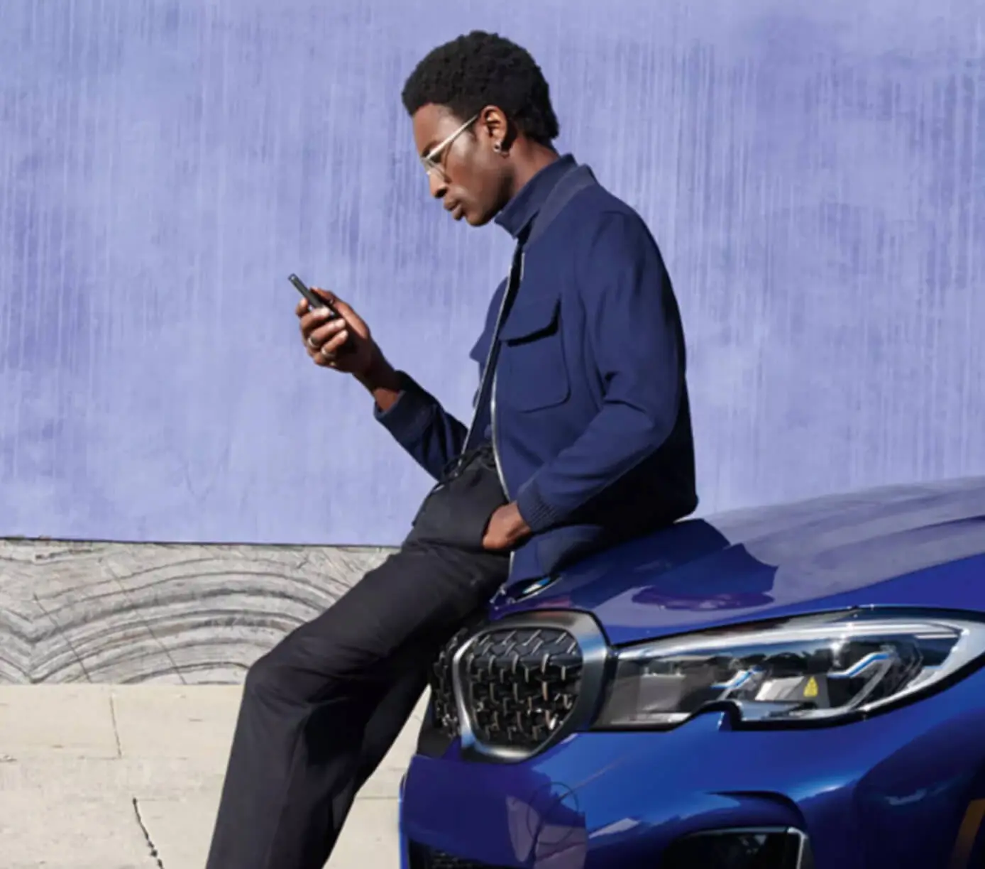 A man leans on a BMW hood while looking at his phone.