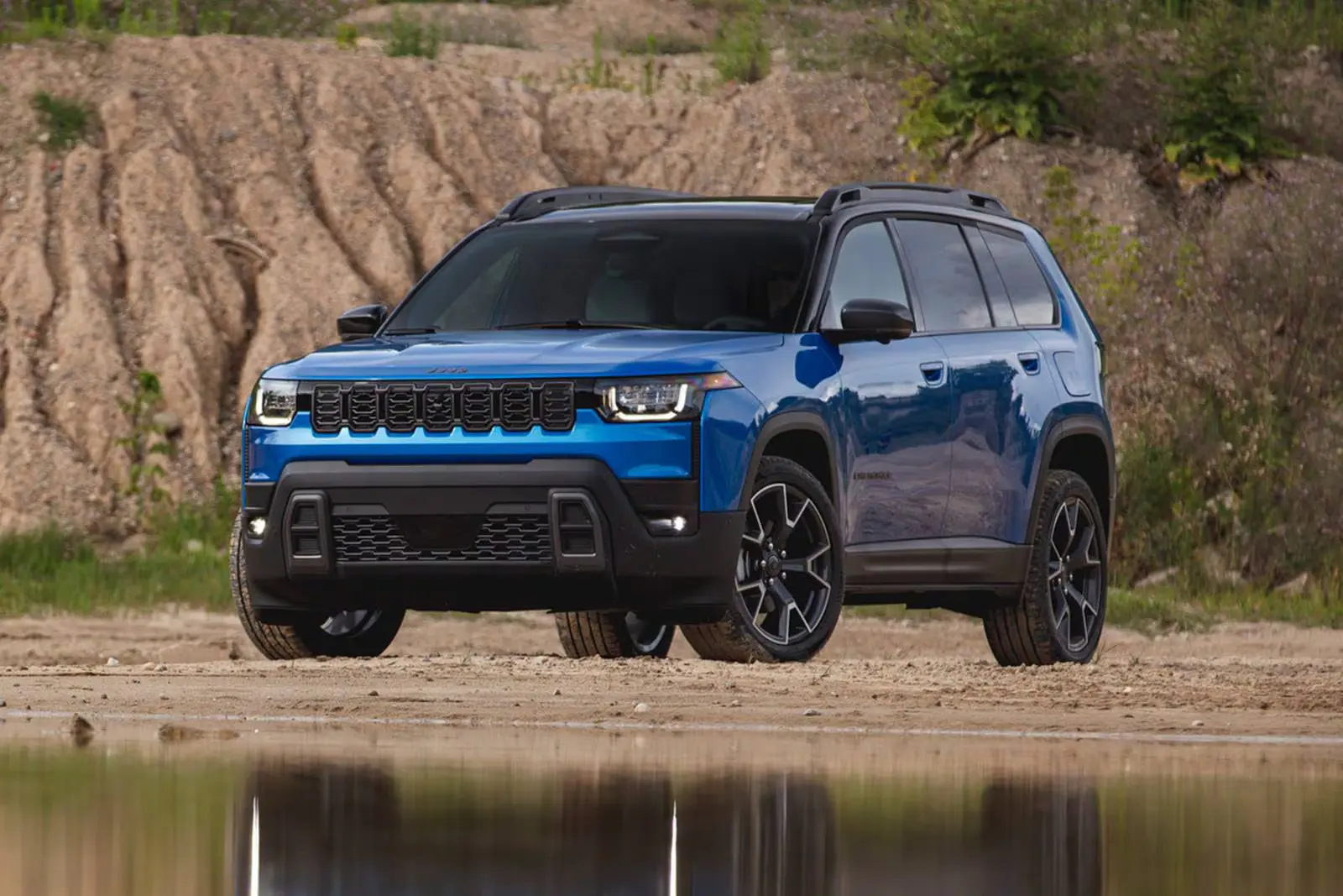 A 2026 blue Jeep Cherokee parked next to a reflective pond in a deserted valley.