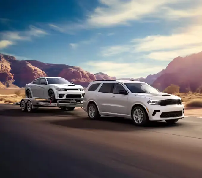 A white durango pulling a car on a trailer.