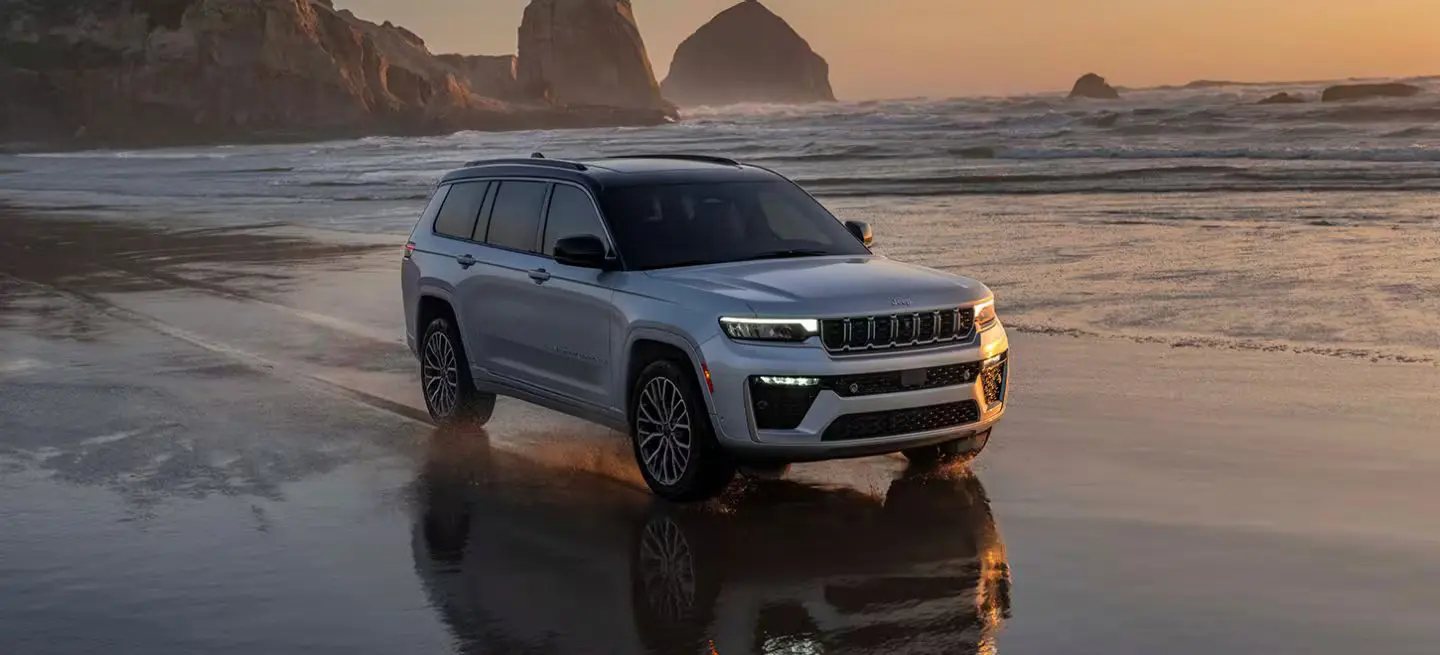 A gray jeep grand cherokee driving on the beach.