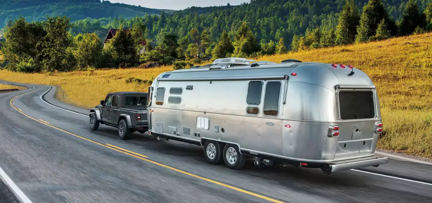 A gray jeep pulling a trailer.
