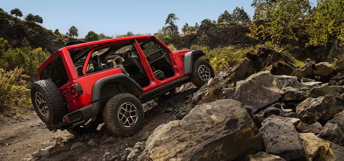 A red jeep driving up some rocks.