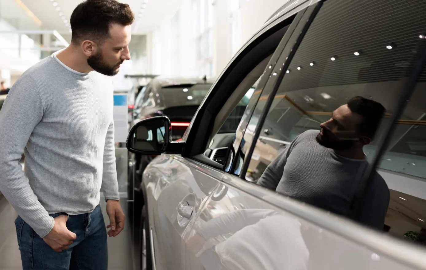 Man examining a vehicle in a dealership showroom.
