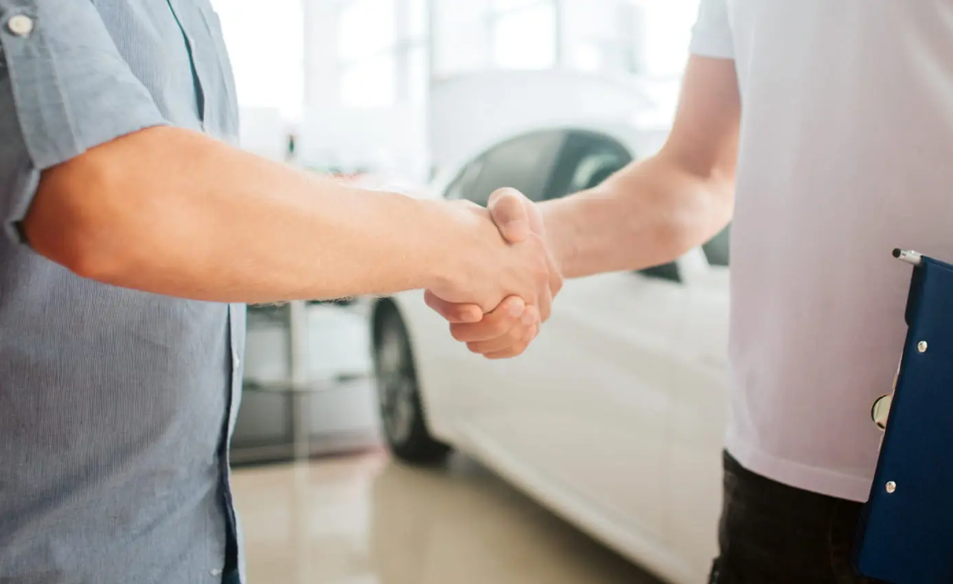 Two people shaking hands at a car dealership.