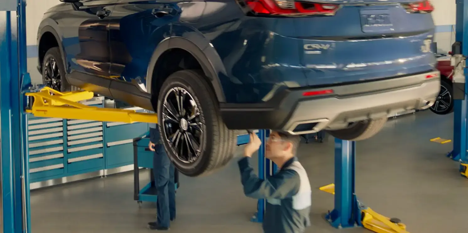 Technician inspecting a Honda SUV on a lift in a service bay.