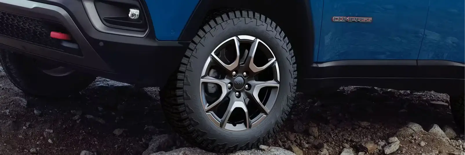 Close-up of Jeep SUV wheel and tire on rocky terrain.