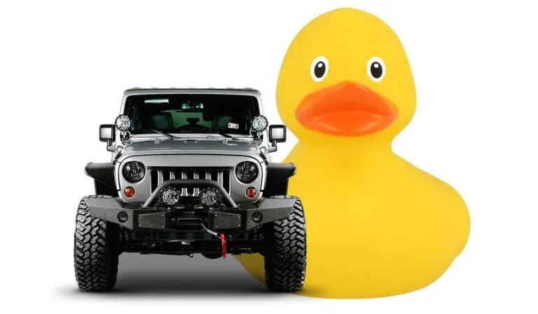 A Large Yellow rubber Duck next to a silver Jeep Wrangler with a white backdrop