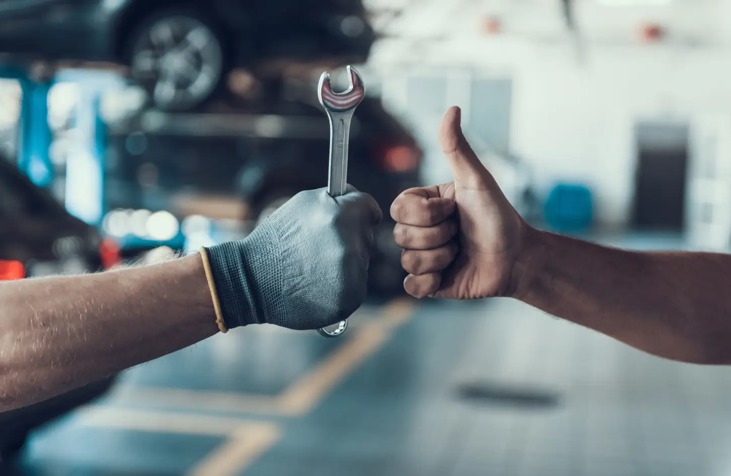 Technician holding a wrench while a customer gives a thumbs up during vehicle service.