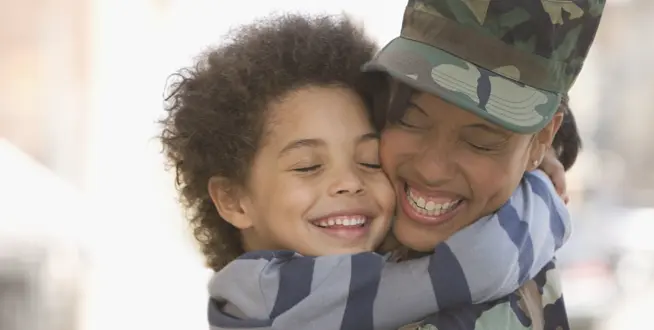 Service member in uniform hugging her smiling son