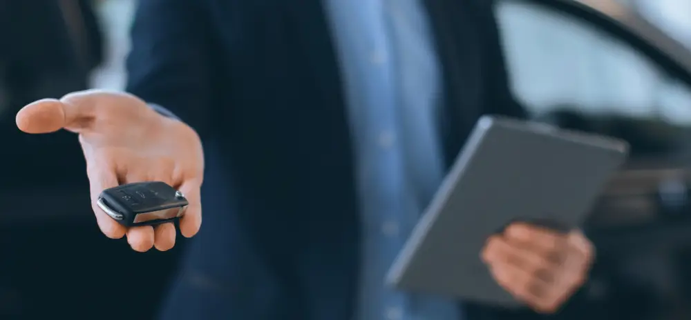 Dealership representative offering car keys to a customer using a tablet