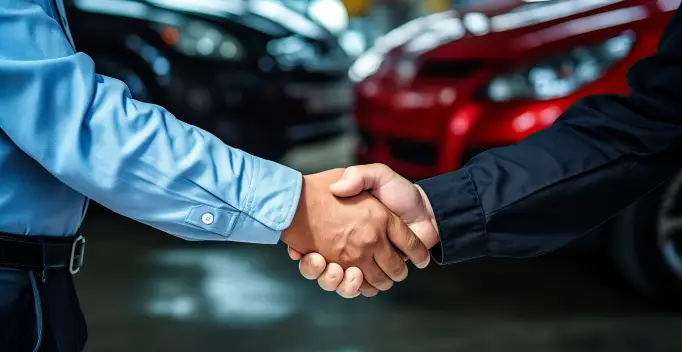 Customer and dealership representative shaking hands in front of vehicles inside a car showroom