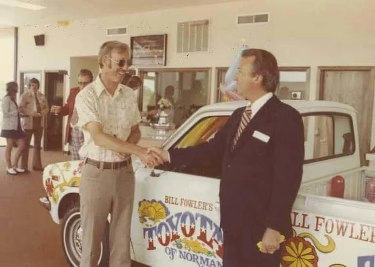 Historic photo of the Fowler family dealership legacy with two men shaking hands beside a Toyota vehicle