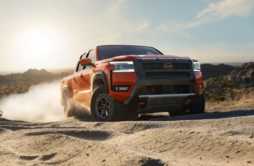 Orange 2026 Nissan Frontier driving off-road on a dusty trail