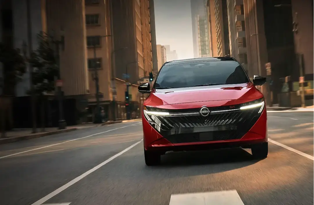 Red 2026 Nissan Sentra driving through downtown traffic
