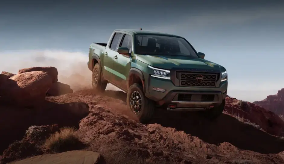 Green Nissan pickup truck driving over rocky off-road terrain.