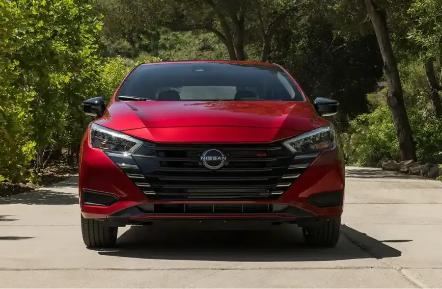 Front view of a red Nissan sedan parked on a tree-lined road