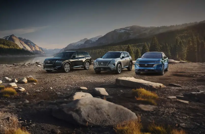 Three Nissan SUVs parked along a mountain lakeshore at dusk