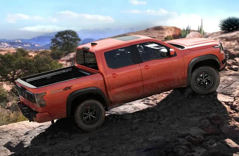 Orange Nissan pickup truck climbing rocky desert terrain