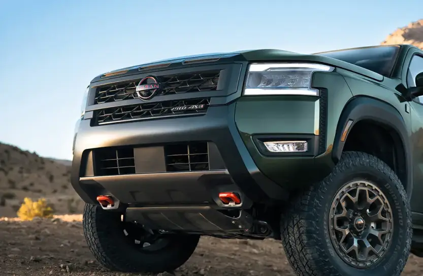 Close-up of a dark green Nissan pickup truck's front grille in the desert