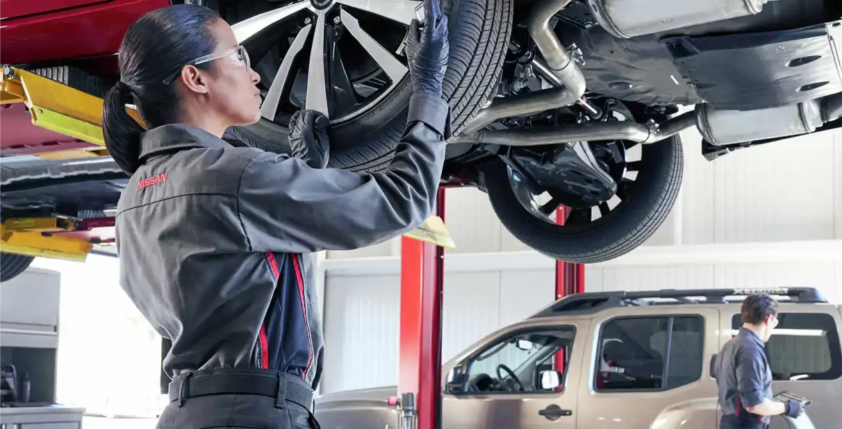 Nissan technician inspecting a tire from underneath a lifted vehicle