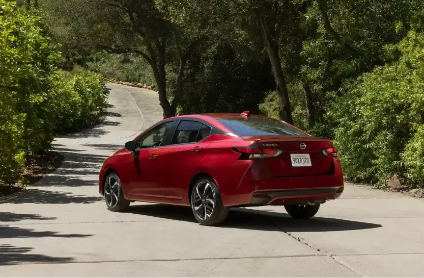 Red Nissan Versa driving on a winding tree-lined road
