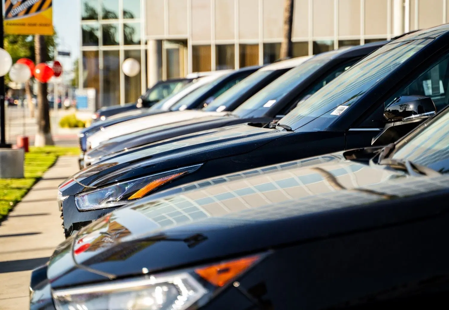 A used mid-size sedan in a sunlit driveway shows wear from different previous owners: kids’ items, trade tools, and personal touches. Details include scuffed seats, dashboard fingerprints, toolbox, soccer ball, booster seat, faded air freshener, and subtle exterior blemishes.