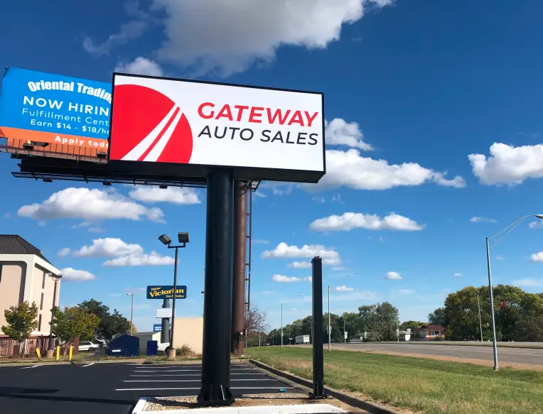 Gateway Auto Sales billboard sign by roadside under blue sky.
