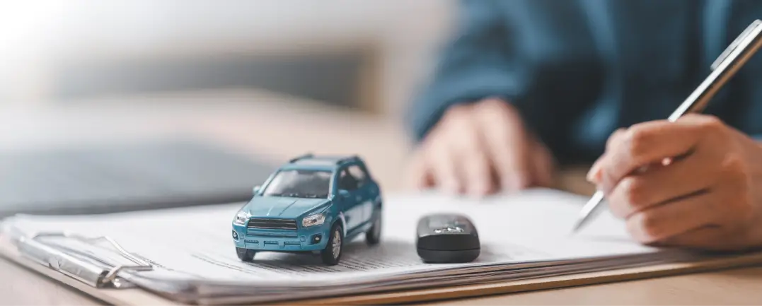 Person signing car purchase paperwork with car key and miniature vehicle on documents