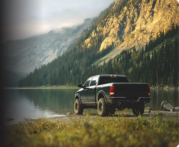 Black pickup truck parked beside a mountain lake with forest and rocky cliffs.